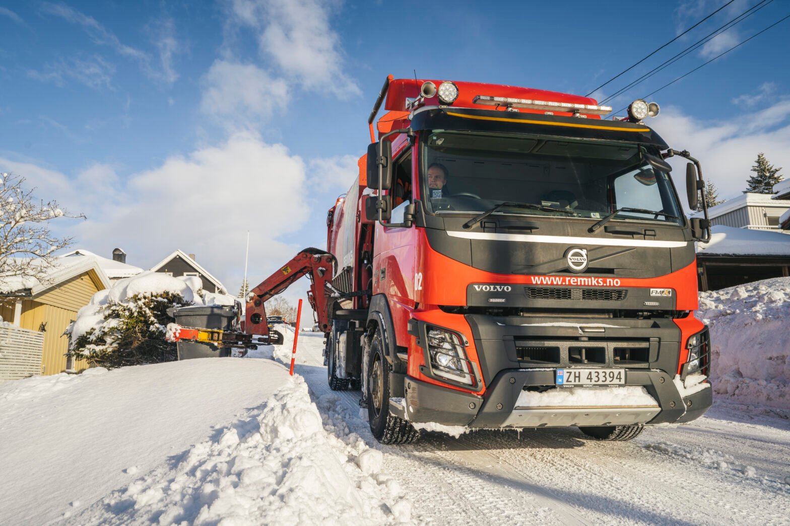 renovasjonsbil som henter avfall i sol og vinter.